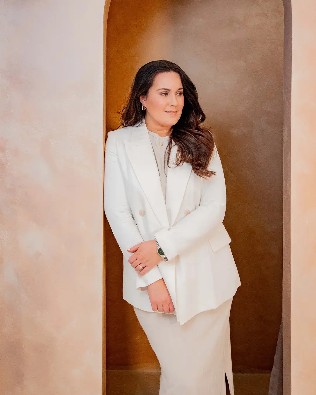 Beth Hobbs in a white suit, standing in an arched alcove
